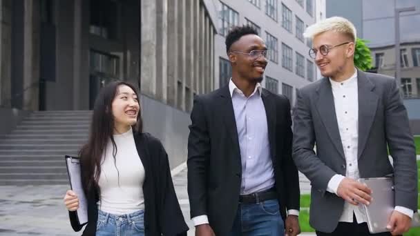 Snygga nöjda blandade ras kontorsarbetare promenader nära stadsbyggnad och poserar på kamera med gemensamma kramar — Stockvideo
