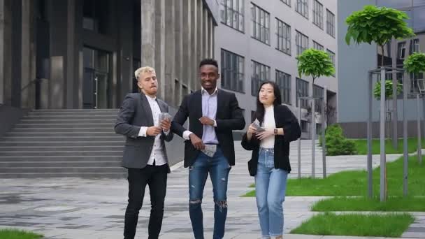 Front view of good-looking high-spirited young multiracial mates which throwing up money over their heads and dancing in the street — Stock Video