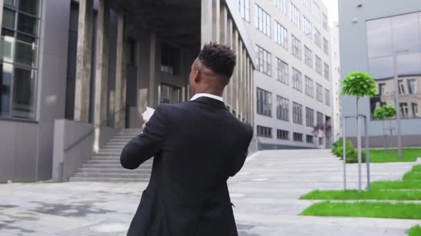 Agradable afortunado rico hombre de piel negra de moda bailando en la calle cerca de un edificio moderno y la dispersión de billetes de cien dólares — Vídeo de stock