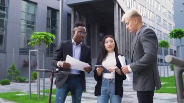 Çekici içerikli, çalışkan, çok ırklı arkadaşlar açık havada çalışıyor ve i-pad 'den gelen mali belgeleri ve verileri karşılaştırıyor.