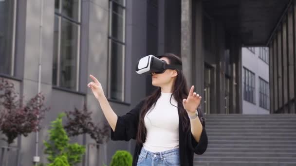 Tilltalande allvarliga målmedveten ung asiatisk kvinna som arbetar på virtuell skärm i augmented reality glasögon nära moderna kontorsbyggnad — Stockvideo