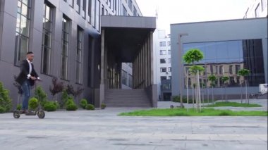 Yakışıklı, kendine güvenen, modaya uygun genç Afrikalı Amerikalı güzel şehir binalarının yakınında e-scooterla geziyor.