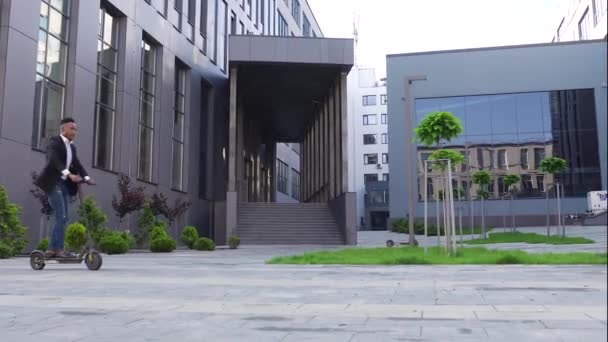 Snygg självsäker modern afrikansk amerikan i trendig slitage ridning på e-scooter nära vackra stadsbyggnader — Stockvideo