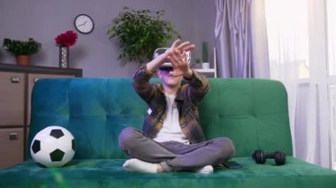 Yakışıklı, gülümseyen, 10 yaşında, özel 3D gözlüklü çocuk evde video oyunu oynarken sanal ekranda ellerini hareket ettiriyor.