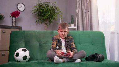 Yakışıklı, konsantre genç çocuk evdeki rahat koltukta oturuyor ve video oyunu oynarken joystick uyguluyor.