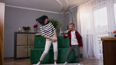 Gülen, gülümseyen, sevimli anne ve oğlu ile birlikte eğlenen ve evde dans eden disko hareketlerini yapan komik gülümsemeye yakın.