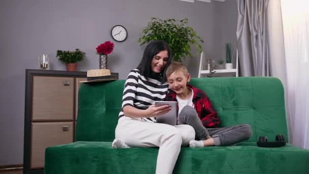 Närbild av attraktiva glada bekymmerslösa mor och son som tillbringar sin fritid tillsammans på att titta på roliga tecknad film eller video på tablet pc hemma — Stockvideo