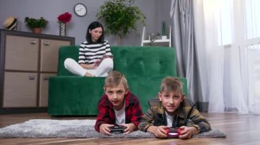İki yakışıklı, kaygısız oğlu yerde video oyunu oynarken güzel gülümseyen genç bayanın koltukta oturup i-pad kullanmasına yakın durun.