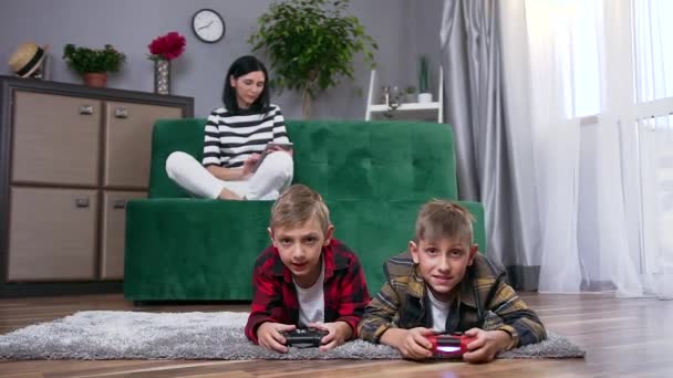 Primo piano di bella sorridente giovane donna seduta sul divano e utilizzando i-pad mentre i suoi due felici bei figli spensierati giocare al videogioco sul pavimento — Video Stock