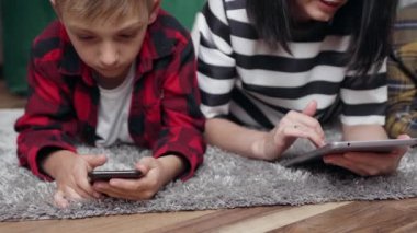 Anne ve iki oğlu evde yerde dinleniyor ve i-pad 'de ilginç videolar izliyorlar.