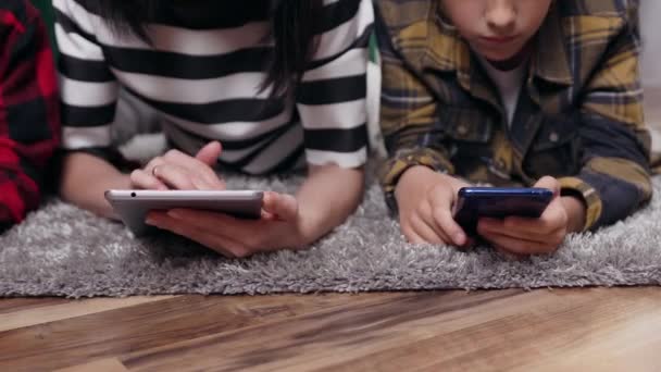 Ferme là. mère amicale et ses deux fils qui reposent ensemble sur le sol et en utilisant des gadgets modernes — Video