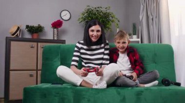 Çekici, mutlu, tedirgin, gülümseyen anne ve oğlunun ön görüntüsü. Koltukta oturup joysticklerle video oyunu oynuyorlar.