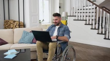 Yakışıklı, güler yüzlü, sakallı, tekerlekli sandalyedeki genç adam laptopta akrabaları ya da arkadaşlarıyla görüntülü görüşme yapıyor.
