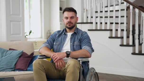 Привабливий концентрований впевнений молодий бородатий сидячий хлопець у інвалідному кріслі, дивлячись на камеру в красиво спроектованому будинку — стокове відео