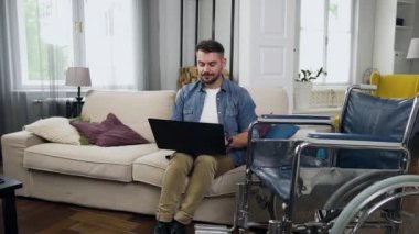 Çekici, pozitif, rahat sakallı, sakallı bir adam evdeki rahat koltukta oturuyor ve bilgisayarla uğraşıyor.