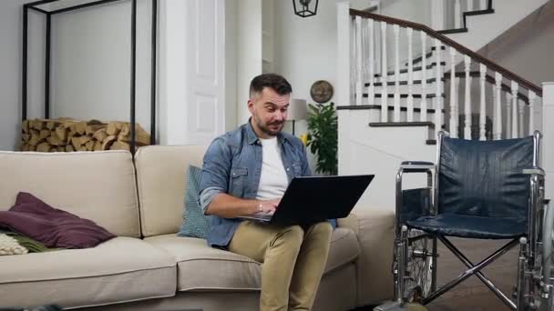 Dobře vypadající spokojený 30-letý vousatý postižený chlap oslavující vítězství poté, co viděl dobré zprávy na obrazovce počítače doma — Stock video