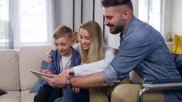 Boa aparência feliz sorrindo pai barbudo moderno em cadeira de rodas, mãe e filho usando i-pad na sala de estar contemporânea — Vídeo de Stock