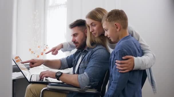 Keluarga dengan gaya modern yang beruntung dan tersenyum sedang menonton di komputer dan berdiskusi di layar dekat jendela besar apartemen sendiri — Stok Video