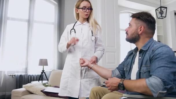Alımlı, sakin, profesyonel kadın tıp asistanı evini ziyaret ederken kalp atışlarını dengeli, sakallı ve tekerlekli sandalyedeki genç adama doğru kontrol ediyor. — Stok video
