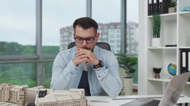 Yakışıklı, ciddi, yüksek yetenekli, sakallı bir mühendis modern tasarım ofisindeki müstakbel binaların projeleriyle ilgili beyin fırtınası yapıyor.