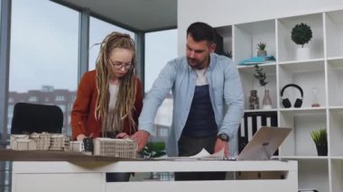 İyi görünümlü profesyonel erkek ve kadın mimarlar modern tasarım ofisindeki yeni binaların planlarıyla birlikte çalışıyorlar.