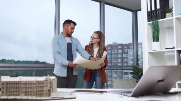 Good-looking ambitious smart modern professional male and female designers standing near the big window in design studio and discussing work moments using blueprint,4k — Stock Video