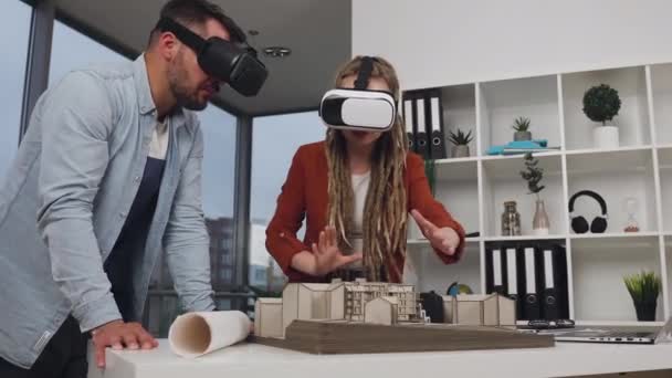 Attraktive selbstbewusste intelligente erfahrene junge Architekten, die in Augmented-Reality-Brillen mit Holzmodell künftiger Gebäude im Designbüro arbeiten — Stockvideo