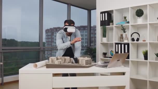 Guapo arquitecto barbudo joven concentrado de alta cualificación en gafas de realidad aumentada trabajando con modelo de edificios en la oficina de arquitectura, 4k — Vídeo de stock