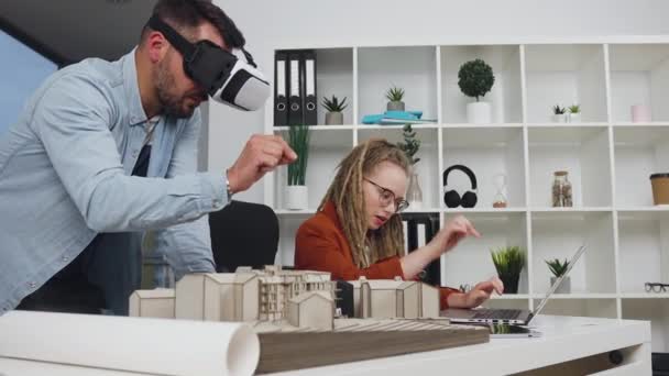 Guapo experimentado propósito joven barbudo arquitecto en gafas especiales 3d hablando con su colega con estilo con rastas que entran en las mediciones de proyectos de nuevos edificios en la computadora — Vídeos de Stock