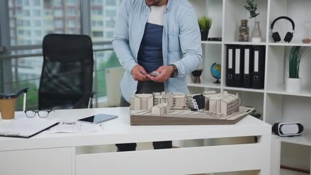 Vonzó, céltudatos, szakállas, 30 éves építész, aki a jövő épületének modelljeivel dolgozik a modern irodaházban. — Stock videók