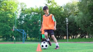 Çekici, kendine güvenen, futbol üniformalı 13 yaşında bir çocuk antrenman gününde yapay yeşil sahada topla futbol oynuyor.