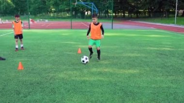 Futbol antrenörü 4K ile ortak ders sırasında futbol sahasında futbol oynamak için antrenman yapan aktif, kendine güvenen gençleri yakın tut.