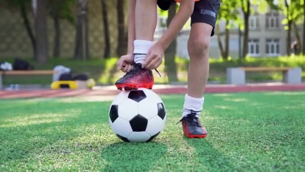 Портрет мальчика-подростка, который завязывает шнурки на спортивной обуви во время игры в футбол на зеленом поле в день тренировки, 4k — стоковое видео