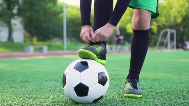 Conceito de futebol onde jogador de futebol amarrando cadarço em suas botas durante o treinamento no campo de futebol, 4k — Vídeo de Stock
