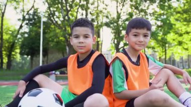 Yeşil sahada oturan ve kameraya bakan iki yakışıklı, kendine güvenen genç çocuğun portresi, 4K