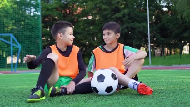 Attrayant satisfait joyeux jeunes amis de football assis sur le terrain de football vert et donnant cinq, regardant la caméra avec de beaux sourires — Video