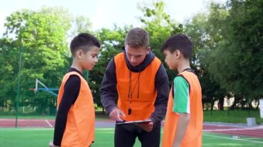 Kendine güveni tam genç bir futbol antrenörü. Bu da yeşil alanda antrenman yaparken iki genç öğrencisine oyunun modelini anlatıyor.