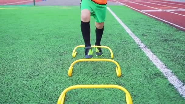 Неизвестный футболист-подросток делает футбольные упражнения с преодолением препятствий во время тренировочного дня на футбольном поле — стоковое видео