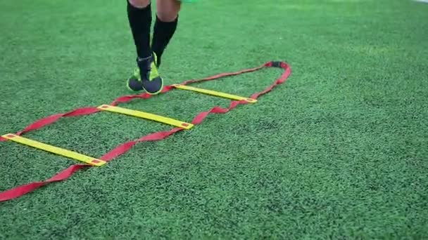 Primer plano de los pies masculinos en zapatos de fútbol que hacen jogging y saltos en la escalera de fútbol durante el entrenamiento en el campo deportivo — Vídeos de Stock