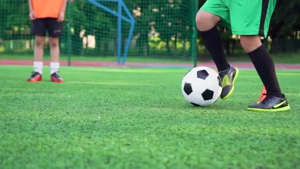 Vista frontal de los pies de los niños en zapatos de fútbol que trabajan con la pelota durante el entrenamiento en el campo de deporte al aire libre — Vídeos de Stock