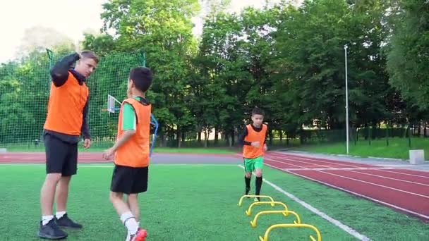 Futbol konsepti, yakışıklı genç futbol antrenörünün futbol sahasındaki engellerle koşmayı bitirdikten sonra öğrencilerine beşlik çakması. — Stok video