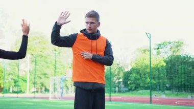 İyi görünümlü genç futbol antrenörü, antrenman sırasında stadyumdaki engellerle antrenman yaptıktan sonra öğrencilerine beşlik çakıyor.