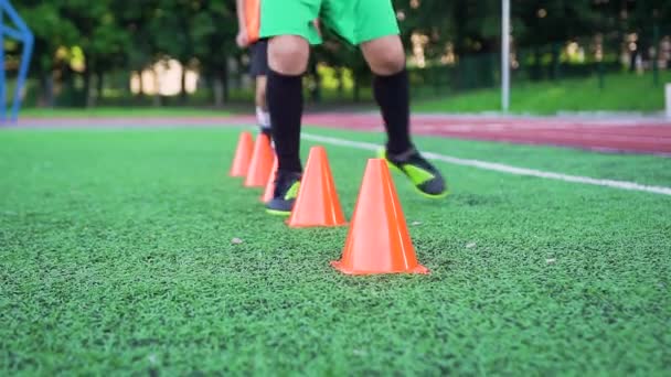 Zbliżenie do stóp piłkarza, że robi ćwiczenia z biegania wokół stojaków dla wytrzymałości podczas treningu na świeżym powietrzu boisko do piłki nożnej — Wideo stockowe