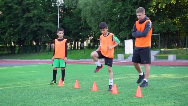 Концентрований висококваліфікований молодий футбольний тренер спостерігає, як його учні роблять стрибки вправи під час тренувань на футбольному полі на відкритому повітрі — стокове відео