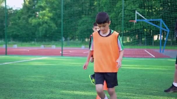 Visão frontal de meninos adolescentes intencionais confiantes em uniformes de futebol que fazem exercícios de corrida com obstáculos com bola no estádio no dia do treinamento — Vídeo de Stock