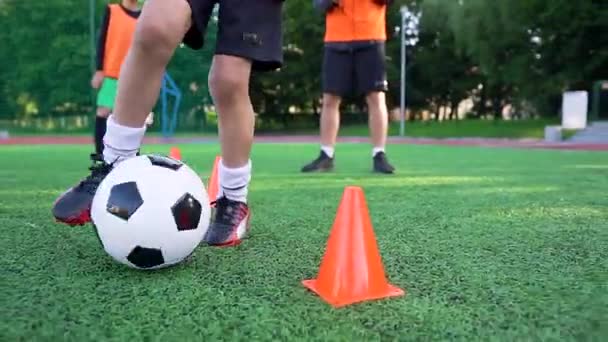 Közelkép a fiúk lábát, hogy fut a labda körül a fogaskerekek a szabadban sportpálya alatt futball edzés napján — Stock videók
