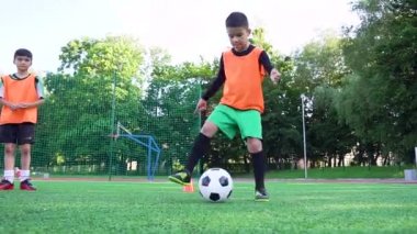 Çekici hareketli, futbol üniformalı genç bir çocuk açık hava spor sahasındaki antrenman sırasında top becerilerini geliştiriyor.