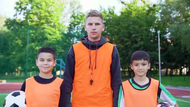 Piacevole sportivo due ragazzi diversi e il loro allenatore altamente qualificato in piedi sul campo di calcio e guardando la fotocamera, vista frontale — Video Stock