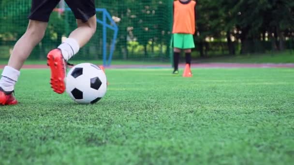 Primer plano de los pies de los niños en zapatos de fútbol que resuelven la patada con la pelota durante el día de entrenamiento en el campo deportivo — Vídeos de Stock