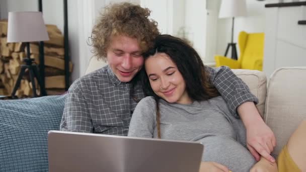 Casamento atraente amoroso jovem casal grávida relaxando no sofá confortável em casa e assistindo fotos da família no laptop — Vídeo de Stock